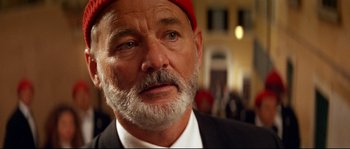 Movie still from “The Life Aquatic with Steve Zissou” (2004), directed by Wes Anderson – A person wearing a suit and a red hat; Close Up shot, Low angle