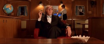 Movie still from “The Life Aquatic with Steve Zissou” (2004), directed by Wes Anderson – An older man sitting in a chair smoking a cigarette; Medium shot, Low angle