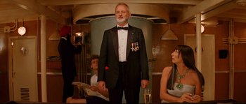 Movie still from “The Life Aquatic with Steve Zissou” (2004), directed by Wes Anderson – An older man in a tuxedo standing in front of two other people; Medium shot, Low angle