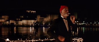 Movie still from “The Life Aquatic with Steve Zissou” (2004), directed by Wes Anderson – An older man smoking a cigarette in front of a body of water at night; Medium shot, Low angle