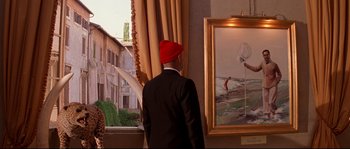 Movie still from “The Life Aquatic with Steve Zissou” (2004), directed by Wes Anderson – A man wearing a red hat looking at a painting; Medium shot, Over the shoulder angle