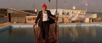 Movie still from “The Life Aquatic with Steve Zissou” (2004), directed by Wes Anderson – An old man in a red hat and a suit is walking across a bridge; Wide shot, Low angle