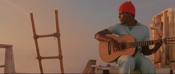 Movie still from “The Life Aquatic with Steve Zissou” (2004), directed by Wes Anderson – A man playing a guitar on top of a wooden platform; Medium shot, Low angle