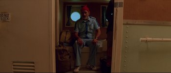 Movie still from “The Life Aquatic with Steve Zissou” (2004), directed by Wes Anderson – A man sitting on a bench in front of a window; Wide shot, Low angle