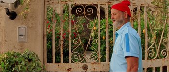 Movie still from “The Life Aquatic with Steve Zissou” (2004), directed by Wes Anderson – An older man wearing a red hat standing in front of an iron gate; Medium shot, Over the shoulder angle