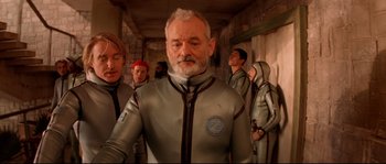 Movie still from “The Life Aquatic with Steve Zissou” (2004), directed by Wes Anderson – A group of people in a room with a man in a silver suit; Medium shot, Low angle