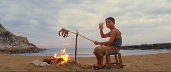 Movie still from “The Life Aquatic with Steve Zissou” (2004), directed by Wes Anderson – A man sitting on a chair next to a fire on the beach; Wide shot, Low angle
