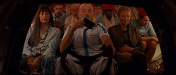 Movie still from “The Life Aquatic with Steve Zissou” (2004), directed by Wes Anderson – An old man sitting in a chair drinking a beverage; Medium shot, Over the shoulder angle