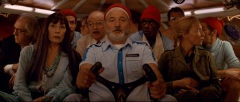Movie still from “The Life Aquatic with Steve Zissou” (2004), directed by Wes Anderson – A group of people riding on a bus with a man riding a bicycle; Medium shot, Low angle