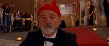 Movie still from “The Life Aquatic with Steve Zissou” (2004), directed by Wes Anderson – A person wearing a suit and a red hat; Close Up shot, Low angle