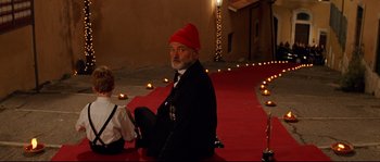 Movie still from “The Life Aquatic with Steve Zissou” (2004), directed by Wes Anderson – An old man sitting on the ground wearing a red hat; Medium shot, Over the shoulder angle