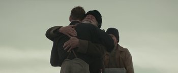 Movie still from “The Light Between Oceans” (2016), directed by Derek Cianfrance – Two men hugging each other in front of another man; Medium shot, Over the shoulder angle