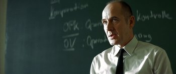 Movie still from “The Lives of Others” (2006), directed by Florian Henckel von Donnersmarck – A man in a white dress shirt and black tie is in front of a blackboard; Close Up shot, Low angle