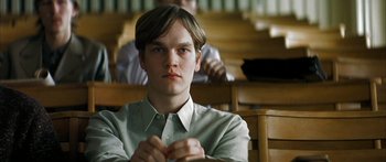 Movie still from “The Lives of Others” (2006), directed by Florian Henckel von Donnersmarck – A man sitting in front of a group of people in a room; Close Up shot, Low angle
