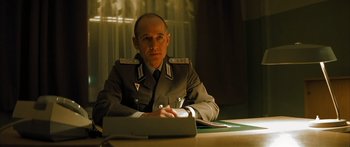 Movie still from “The Lives of Others” (2006), directed by Florian Henckel von Donnersmarck – A man sitting at a table in a uniform; Medium shot, Low angle