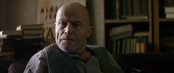 Movie still from “The Lives of Others” (2006), directed by Florian Henckel von Donnersmarck – An older bald man sitting in front of a bookshelf; Close Up shot, Low angle