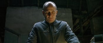 Movie still from “The Lives of Others” (2006), directed by Florian Henckel von Donnersmarck – A bald man in a black jacket is looking down; Close Up shot, Low angle