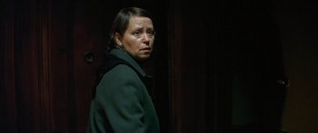 Movie still from “The Lives of Others” (2006), directed by Florian Henckel von Donnersmarck – A woman standing in a dark room looking at the camera; Close Up shot, Over the shoulder angle