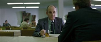 Movie still from “The Lives of Others” (2006), directed by Florian Henckel von Donnersmarck – A man sitting at a table with a drink in front of him; Medium shot, Over the shoulder angle