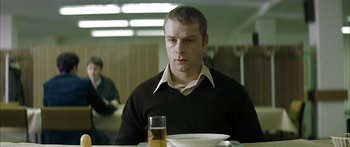 Movie still from “The Lives of Others” (2006), directed by Florian Henckel von Donnersmarck – A man sitting in front of a plate of food; Medium shot, Low angle