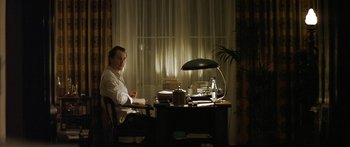 Movie still from “The Lives of Others” (2006), directed by Florian Henckel von Donnersmarck – A man sitting at a desk in front of a desk lamp; Medium shot, Over the shoulder angle