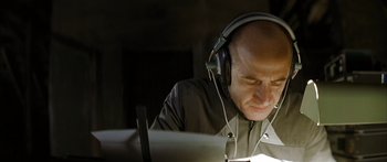 Movie still from “The Lives of Others” (2006), directed by Florian Henckel von Donnersmarck – A bald man wearing headphones looking down at a laptop computer; Close Up shot, Low angle