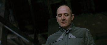 Movie still from “The Lives of Others” (2006), directed by Florian Henckel von Donnersmarck – A bald man in a gray jacket is looking down; Close Up shot, Low angle