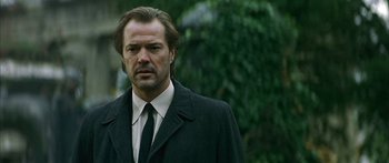 Movie still from “The Lives of Others” (2006), directed by Florian Henckel von Donnersmarck – A man in a suit and tie standing in front of a tree; Close Up shot, Low angle