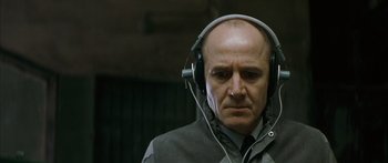 Movie still from “The Lives of Others” (2006), directed by Florian Henckel von Donnersmarck – A bald man wearing headphones and a jacket; Close Up shot, Over the shoulder angle
