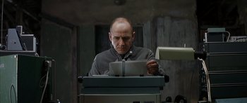 Movie still from “The Lives of Others” (2006), directed by Florian Henckel von Donnersmarck – A man is reading a paper while sitting at a desk; Close Up shot, Low angle