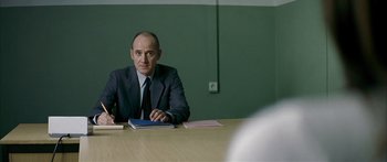 Movie still from “The Lives of Others” (2006), directed by Florian Henckel von Donnersmarck – A man sitting at a table in front of papers; Medium shot, Over the shoulder angle