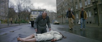 Movie still from “The Lives of Others” (2006), directed by Florian Henckel von Donnersmarck – A person is laying on the ground in the street; Wide shot, Low angle