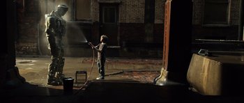 Movie still from “Real Steel” (2011), directed by Shawn Levy – A young boy holding a hose while standing in a building; Wide shot, High angle