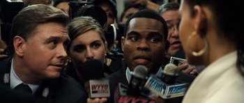 Movie still from “Real Steel” (2011), directed by Shawn Levy – A man and woman are holding microphones in front of a crowd; Close Up shot, Over the shoulder angle