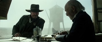 Movie still from “The Lone Ranger” (2013), directed by Gore Verbinski – Two men sitting at a table in front of water tower; Medium shot, Over the shoulder angle