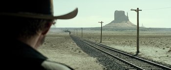 Movie still from “The Lone Ranger” (2013), directed by Gore Verbinski – A person in a cowboy hat riding a train on the tracks; Wide shot, Over the shoulder angle