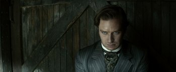 Movie still from “The Lone Ranger” (2013), directed by Gore Verbinski – A man wearing a suit and tie standing in front of a wooden wall; Close Up shot, Low angle