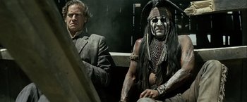 Movie still from “The Lone Ranger” (2013), directed by Gore Verbinski – A man sitting next to a man in a suit; Medium shot, Over the shoulder angle