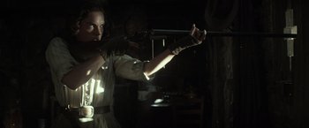 Movie still from “The Lone Ranger” (2013), directed by Gore Verbinski – A woman is holding a gun in a dark room; Medium shot, Over the shoulder angle