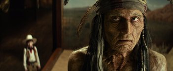 Movie still from “The Lone Ranger” (2013), directed by Gore Verbinski – An old man wearing a feather headdress and looking at the camera; Close Up shot, Low angle