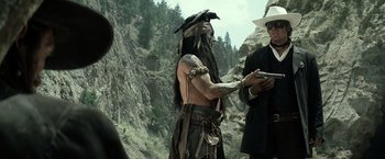 Movie still from “The Lone Ranger” (2013), directed by Gore Verbinski – A man in a native american garb holding a cell phone while standing next to a man in a suit; Medium shot, Over the shoulder angle