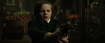 A young boy holding a gun while wearing a suit and tie