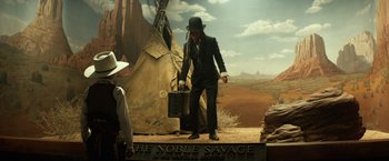 Movie still from “The Lone Ranger” (2013), directed by Gore Verbinski – A man in a black suit and a black hat holding a briefcase in front of a painting; Wide shot, Low angle
