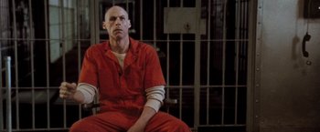 Movie still from “The Long Kiss Goodnight” (1996), directed by Renny Harlin – A man in a red jumpsuit sitting in a jail cell; Medium shot, Low angle