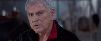 Movie still from “The Long Kiss Goodnight” (1996), directed by Renny Harlin – An older man in a black shirt and red shirt; Close Up shot, Over the shoulder angle