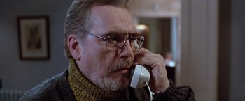 Movie still from “The Long Kiss Goodnight” (1996), directed by Renny Harlin – An older man talking on a phone while wearing glasses; Close Up shot, Low angle