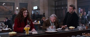 Movie still from “The Long Kiss Goodnight” (1996), directed by Renny Harlin – Two people sitting at a bar with drinks and papers; Medium shot, Over the shoulder angle