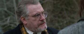 Movie still from “The Long Kiss Goodnight” (1996), directed by Renny Harlin – An older man wearing glasses and a plaid jacket; Close Up shot, Over the shoulder angle