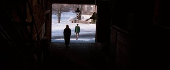 Movie still from “The Long Kiss Goodnight” (1996), directed by Renny Harlin – Two people are walking through a doorway in the snow; Extreme Wide shot, Over the shoulder angle
