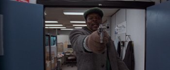 Movie still from “The Long Kiss Goodnight” (1996), directed by Renny Harlin – A man holding a gun in a room with other people; Close Up shot, Low angle